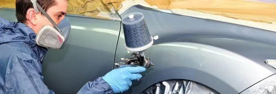 Technician spray-painting a vehicle fender in the paint booth